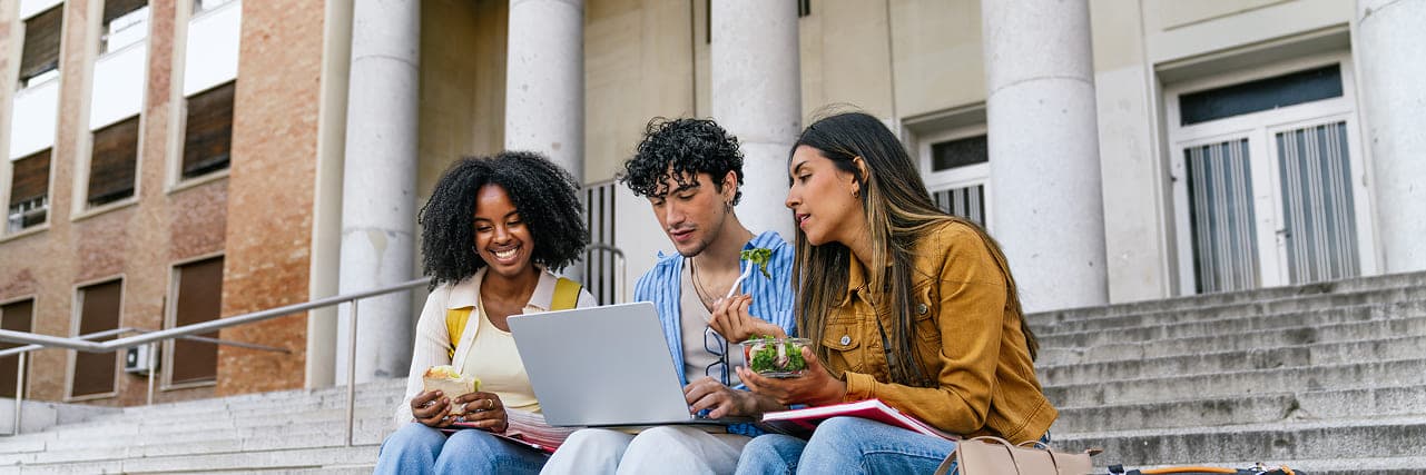 Three students on campus steps sharing a laptop